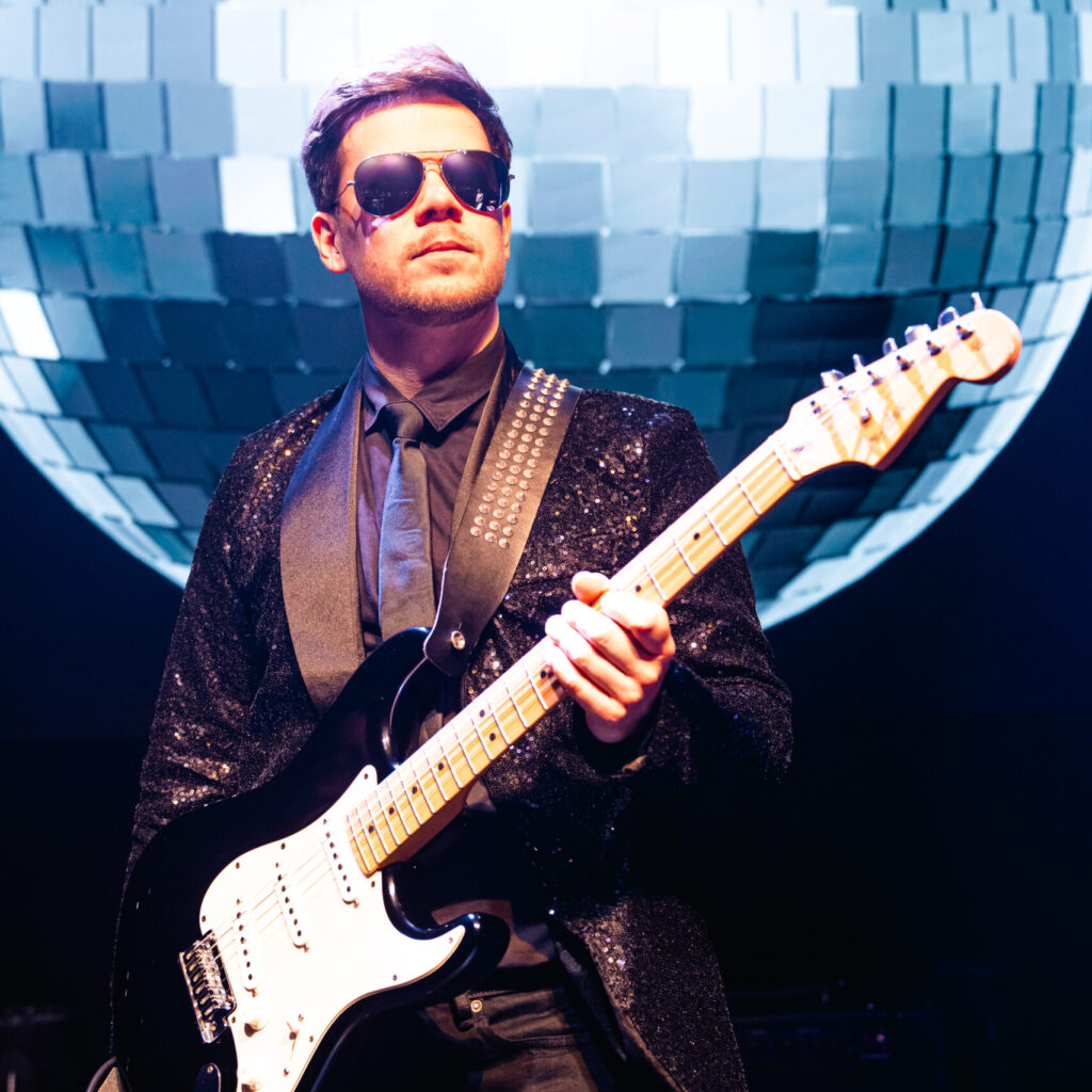 pav guitar player with black guitar behind huge disco ball background